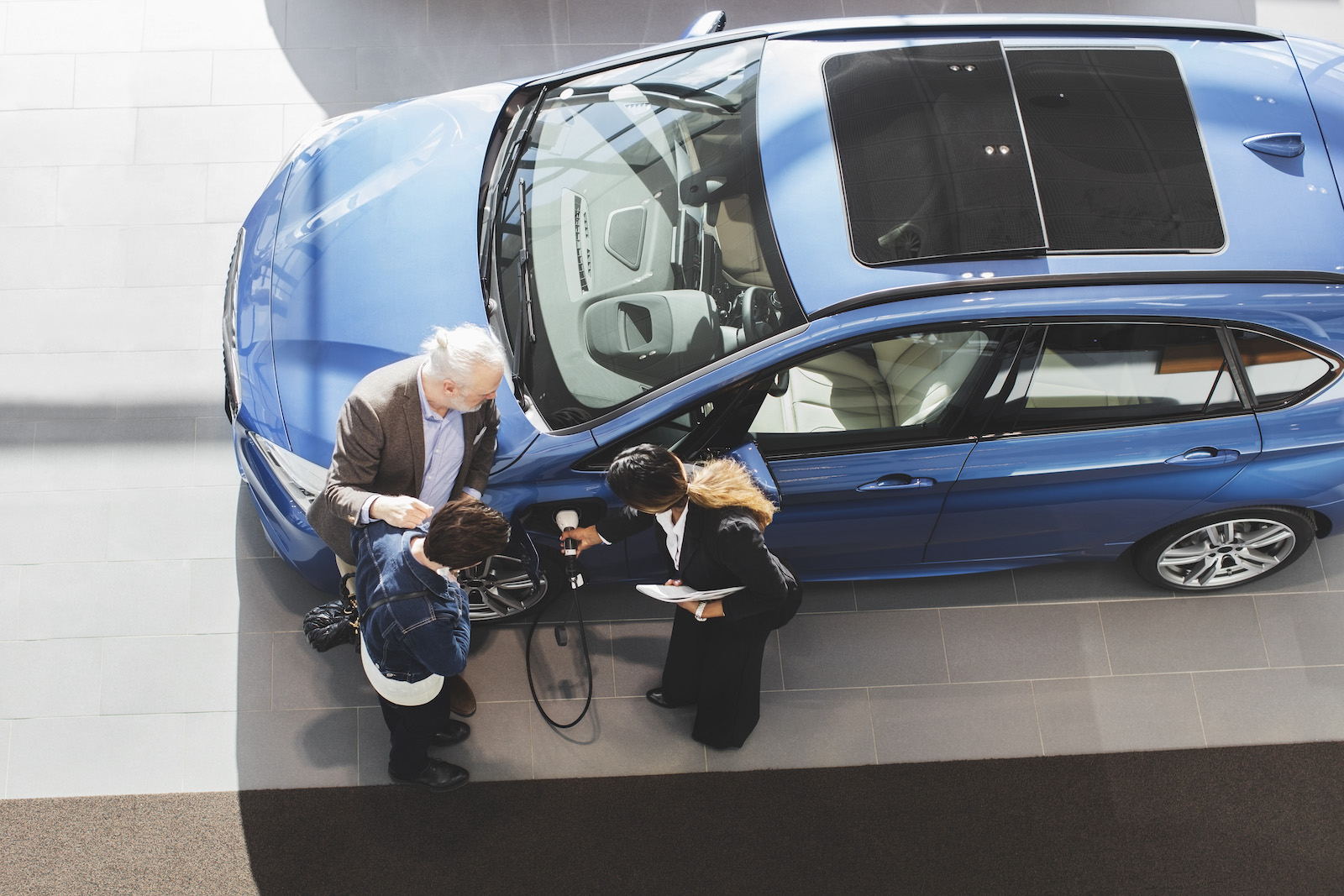 overhead view of saleswoman showing two people an electric vehicle's charging port