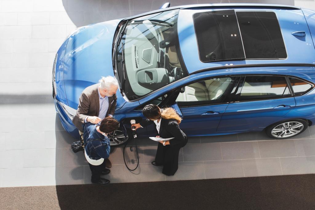 overhead view of saleswoman showing two people an electric vehicle's charging port