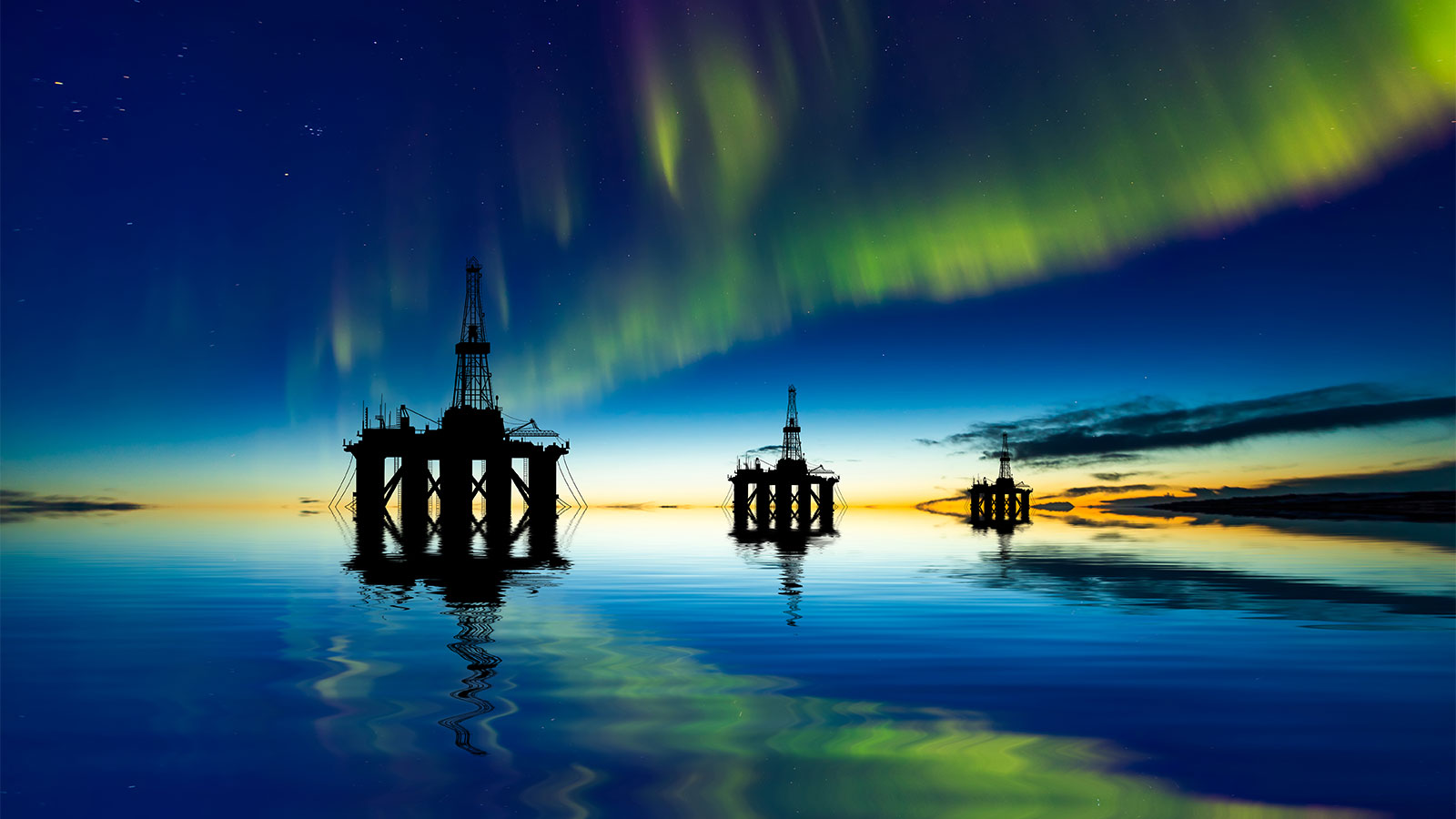 Silhouettes of three offshore oil rigs with the northern lights in the sky above them, and reflected in the water below