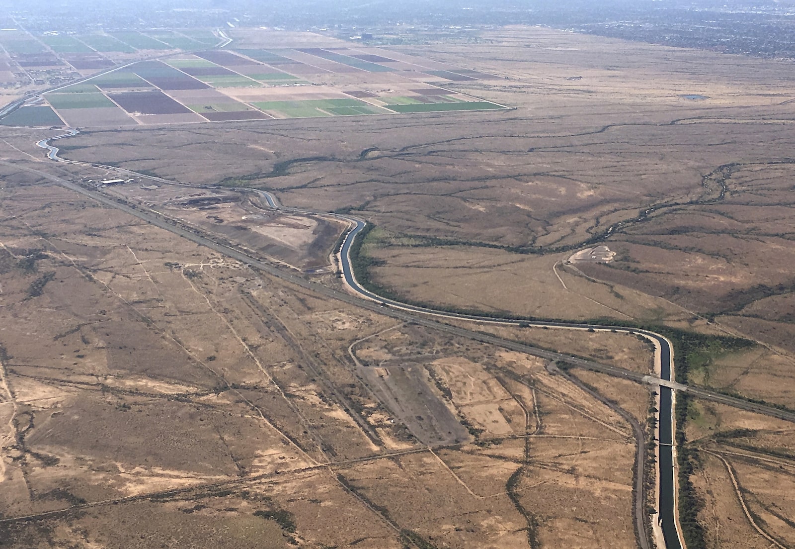 an aerial view of a blue canal winding through dry landcape