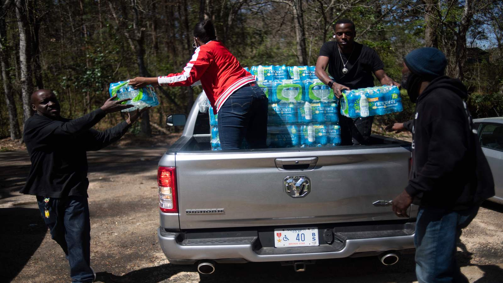 two people hand cases of water out of a pickup truck bed to two other people