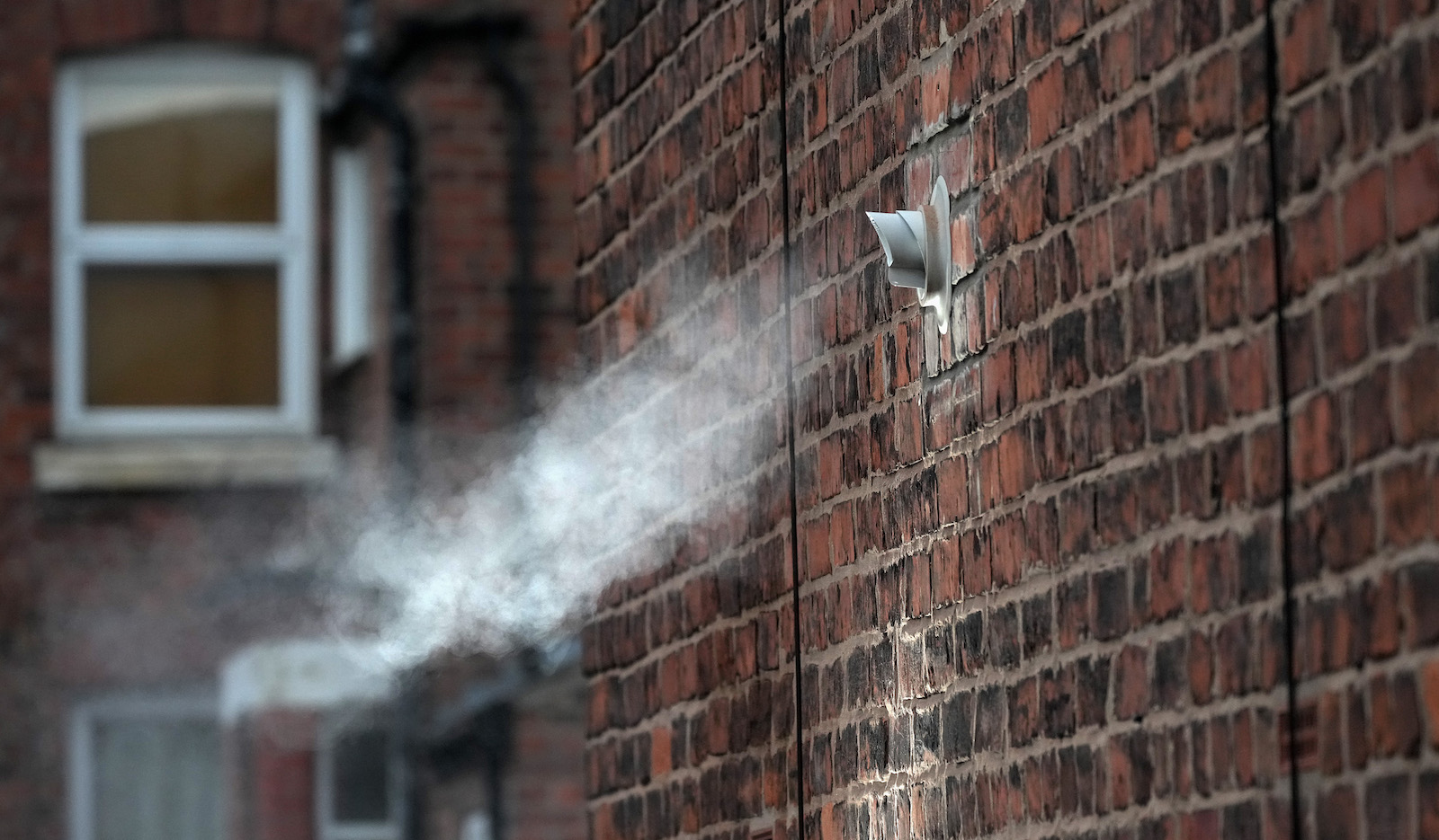 white steam pours out of a flue on the side of a building from a natural gas boiler