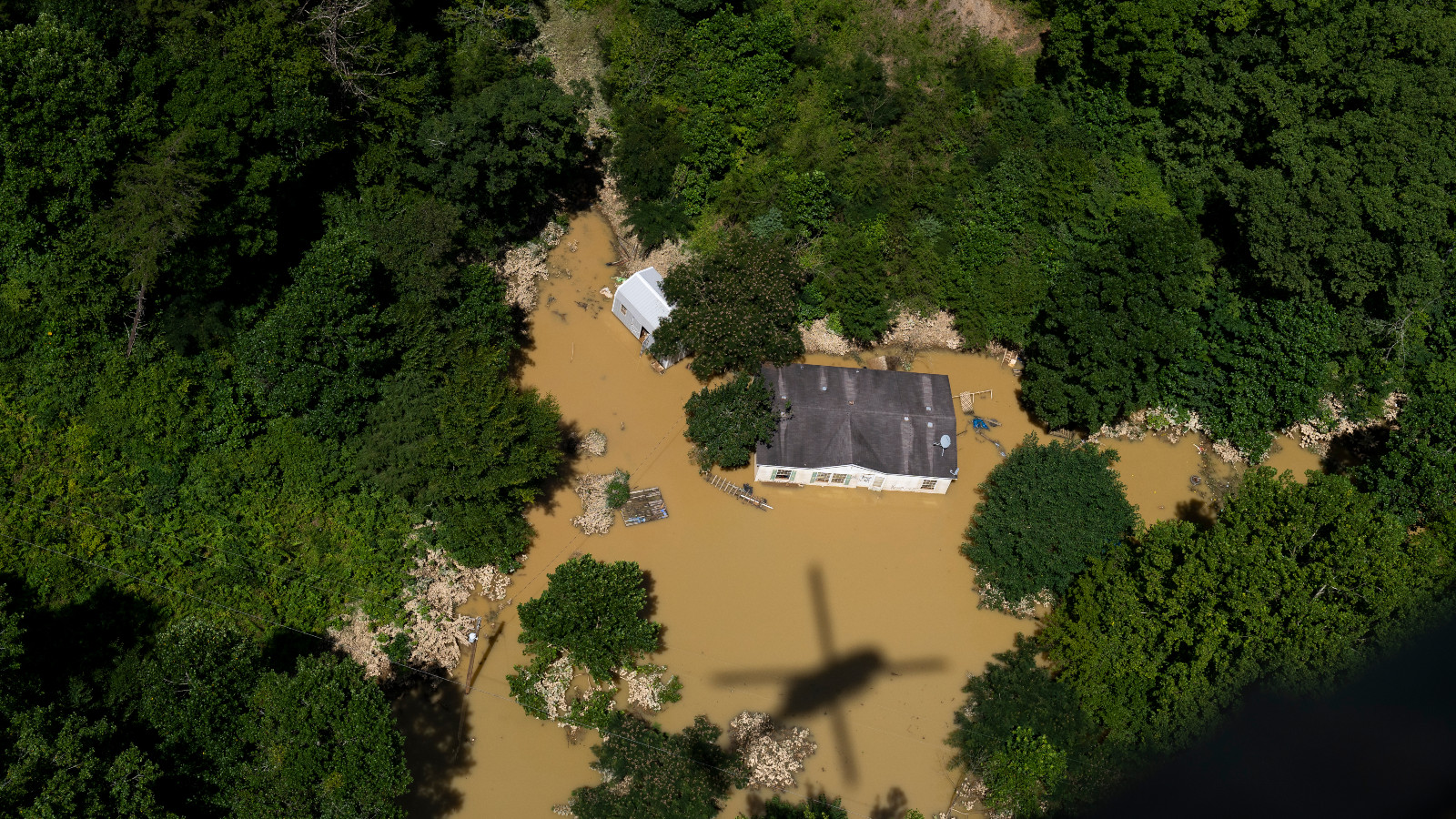 In this aerial view, floodwater surrounds a house as the Kentucky National Guard fly a recon and rescue mission on July 30, 2022 in Breathitt County near Jackson, Kentucky. Flood waters have receded but still surround much of the area. At least 25 people have been killed in the state, with hundreds rescued, but many still unaccounted for amid flooding after heavy rainfall.