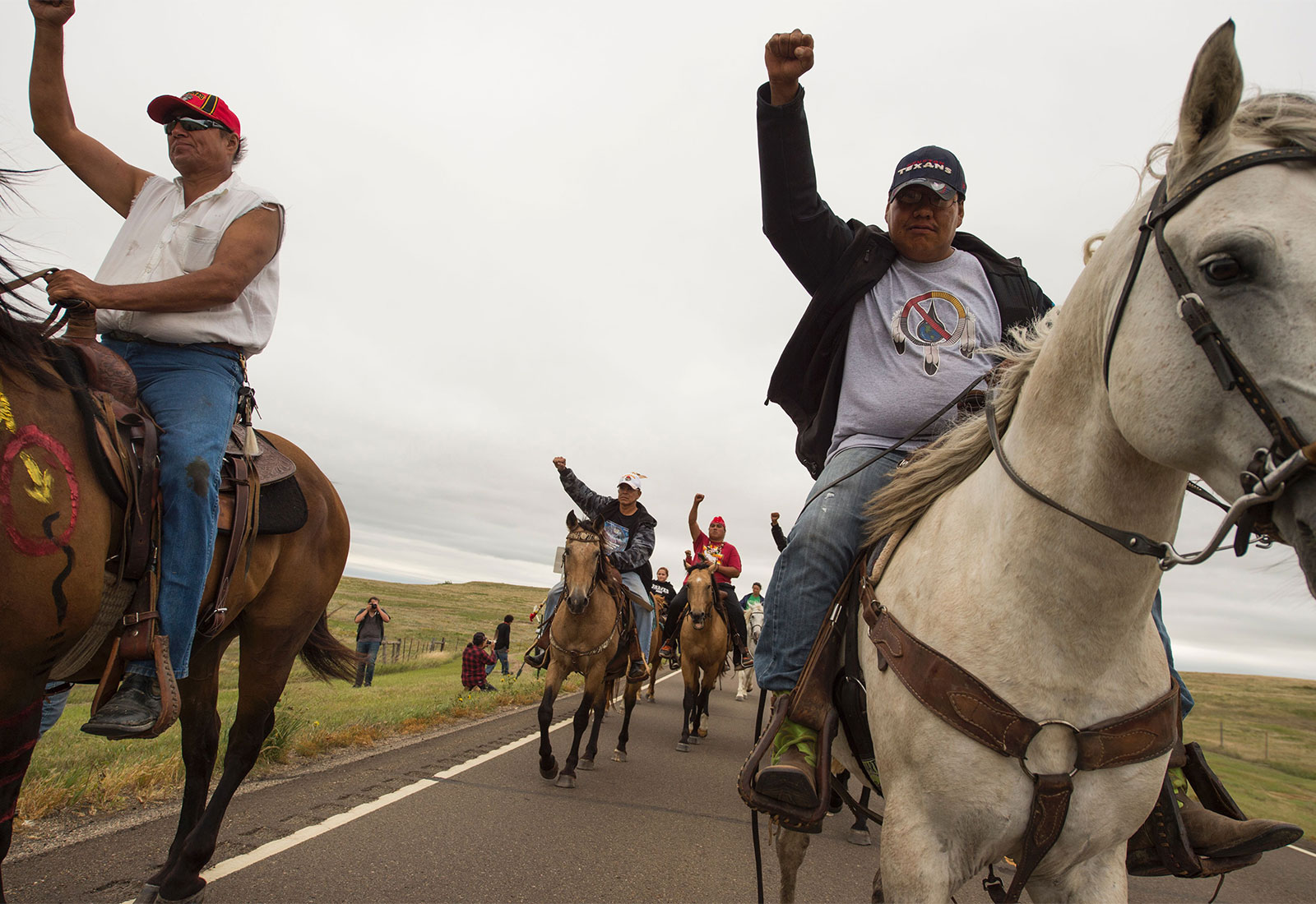 People riding horses raise their fists in protest of the Dakota Access Pipeline