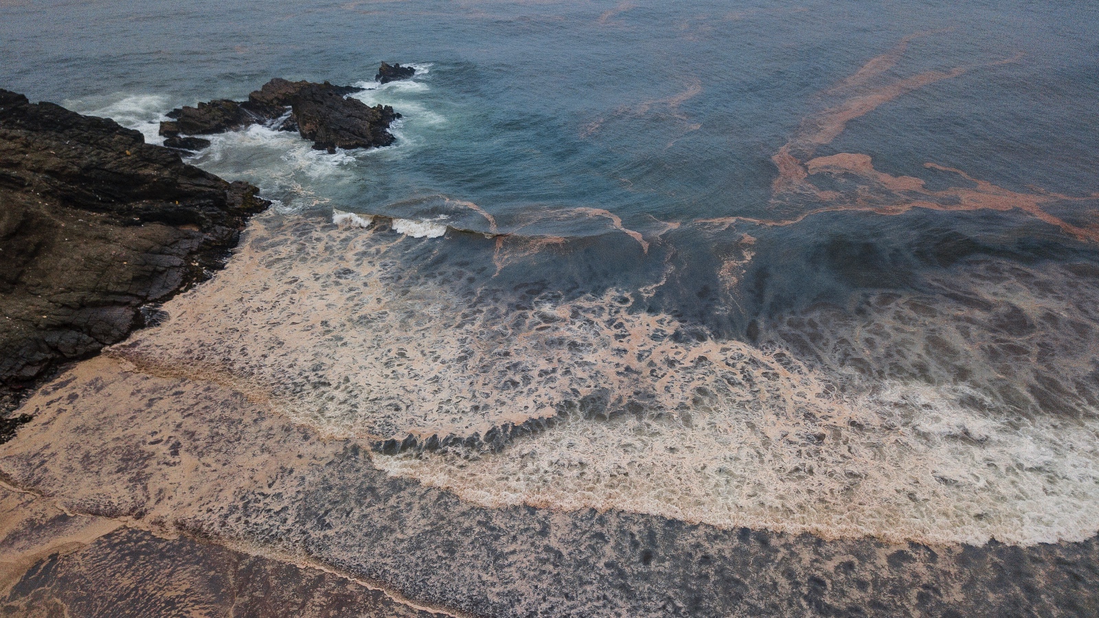 An oil slick turns an ocean and beach brown
