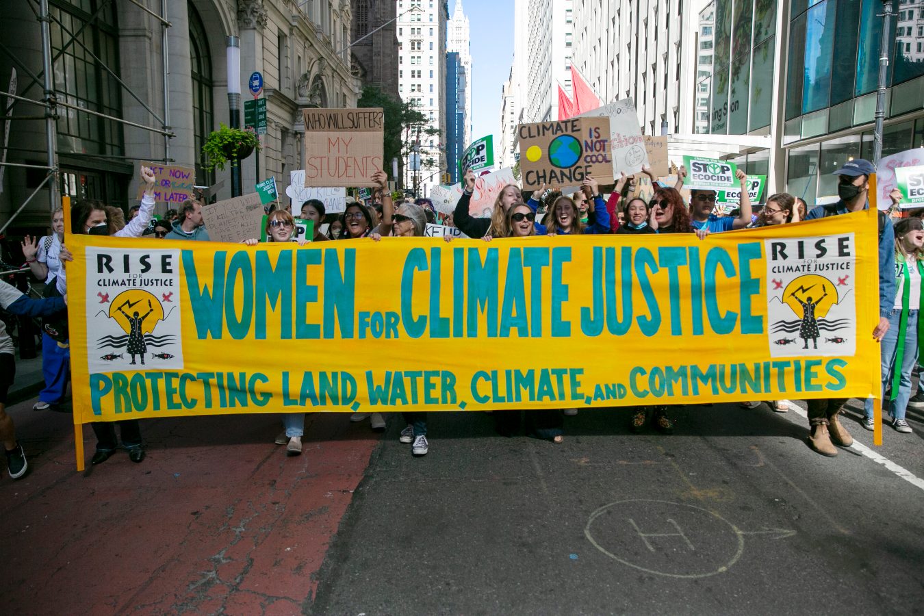 a group of women walk down a city street chanting and carrying a sign for climate justice