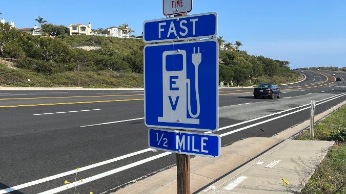 a blue sign for electric vehicle fast charging station along a highway with little traffic