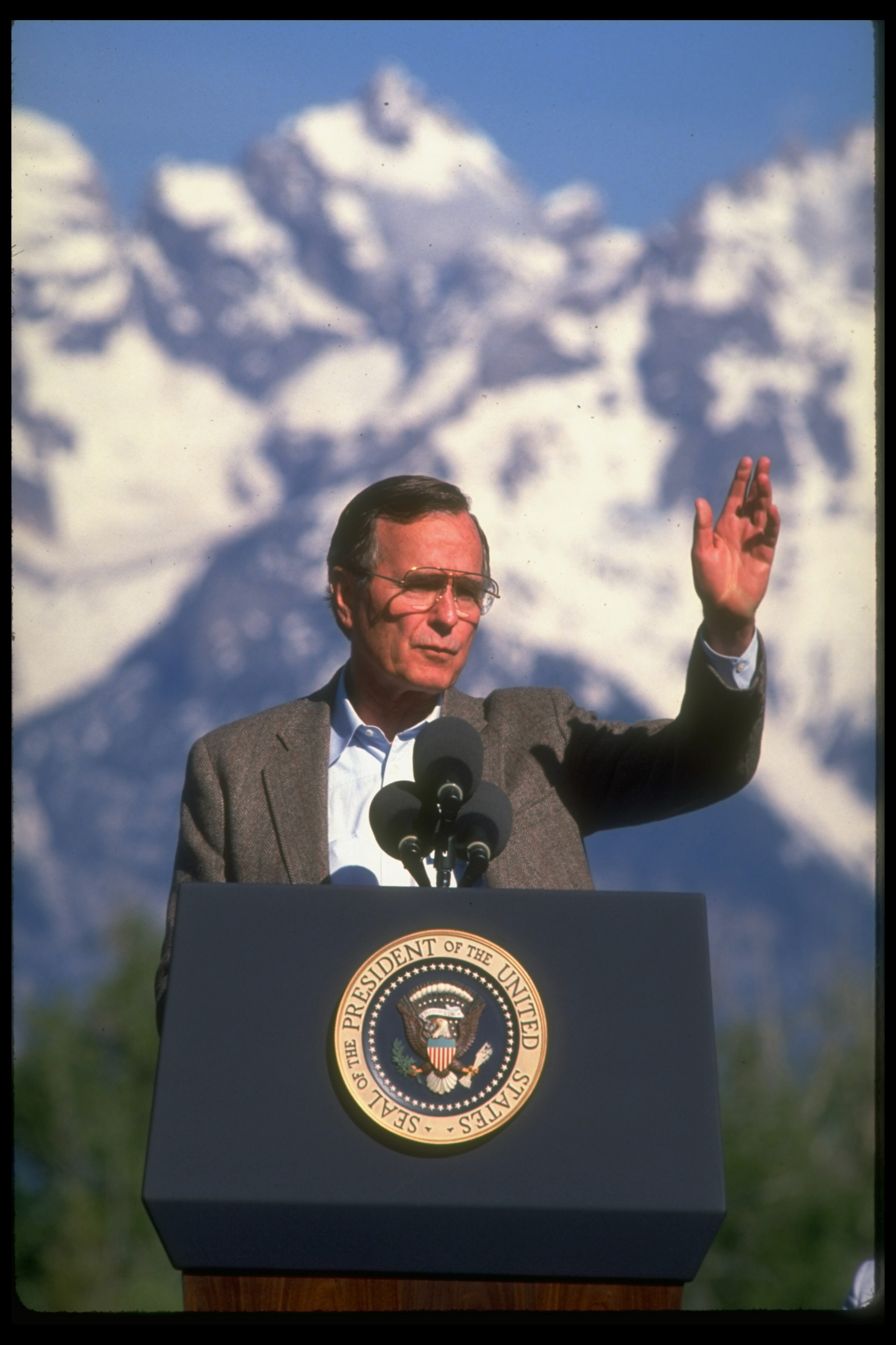 a man (George Bush) stands behind a podium and in front of a snowy mountain