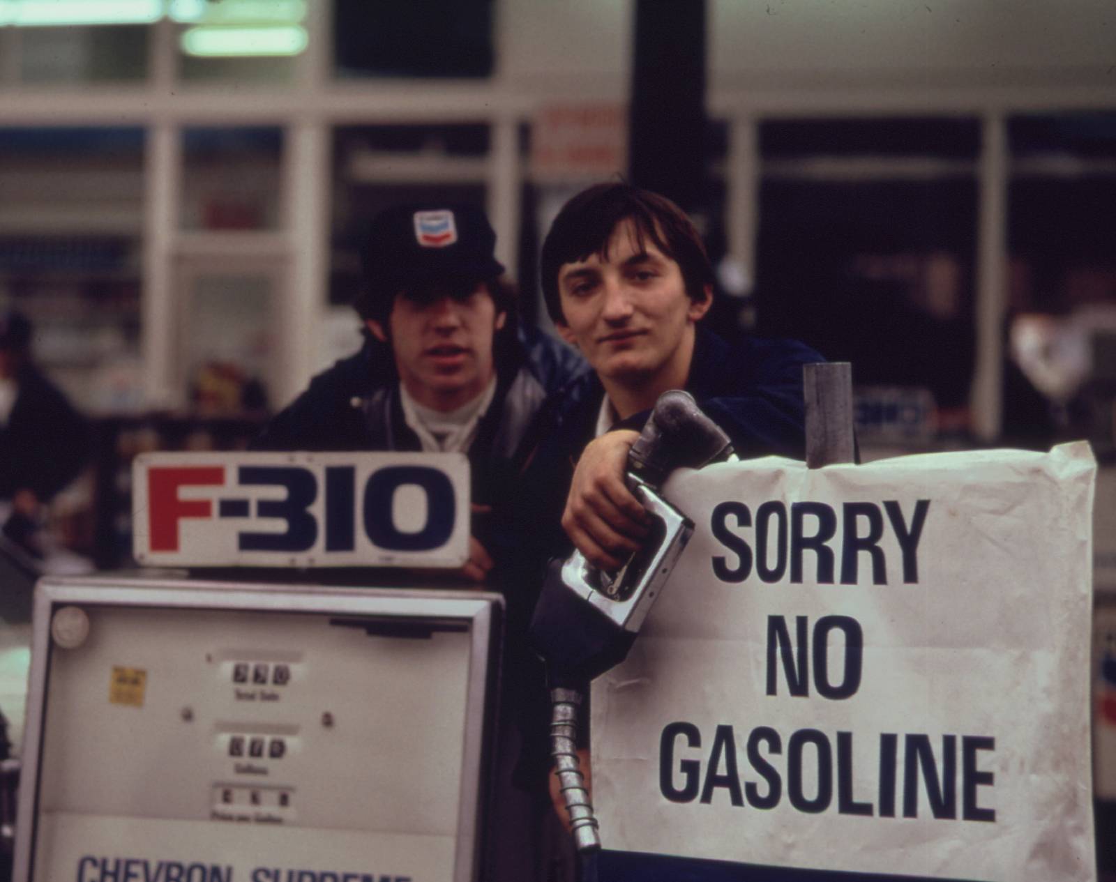 a man holds a sign that says sorry no gasoline next to a pump