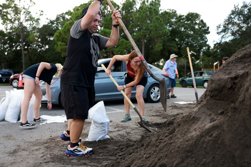 A group of people shovel sand into sandbags in a parking lot
