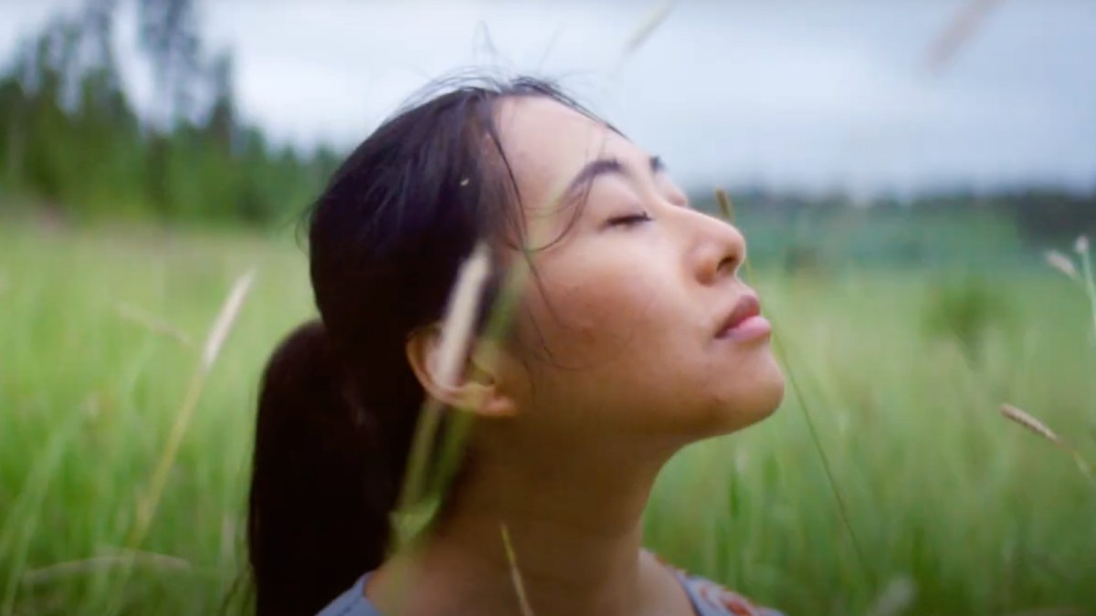 A woman in a meadow looks upward with eyes closed and a peaceful expression