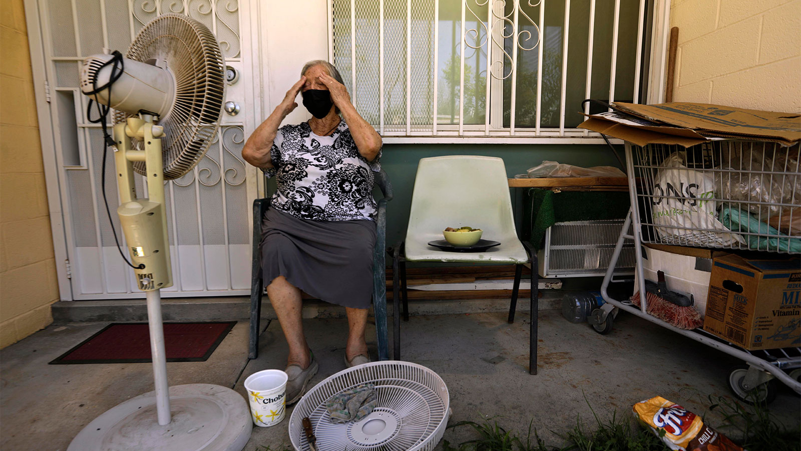Felisa Benitez, an 86 year old woman, wipes the sweat from her brow while taking a break from cleaning her stand-up electrical fan on the porch of her home