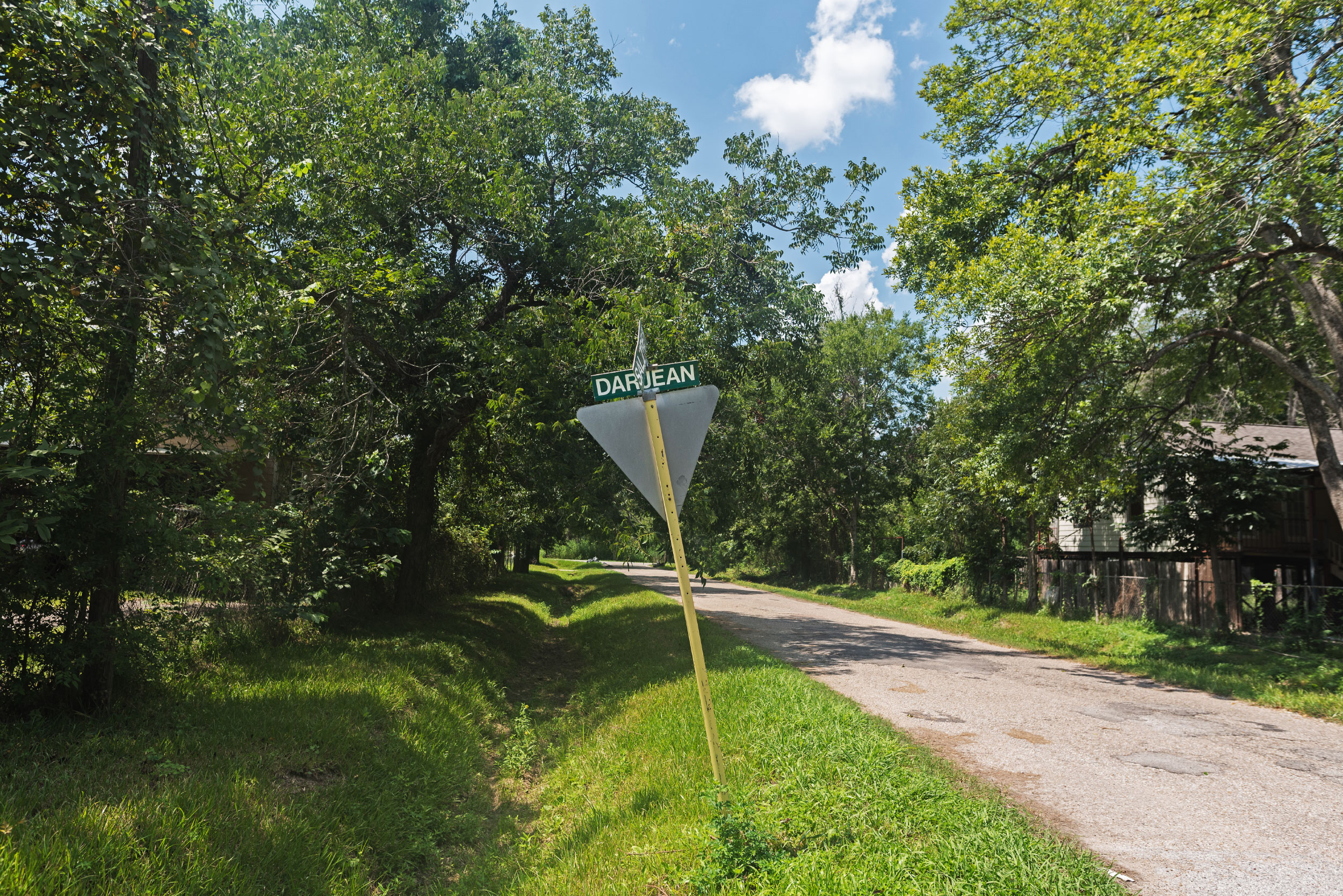 A sign post with the street name Darjean leans toward a grassy ditch