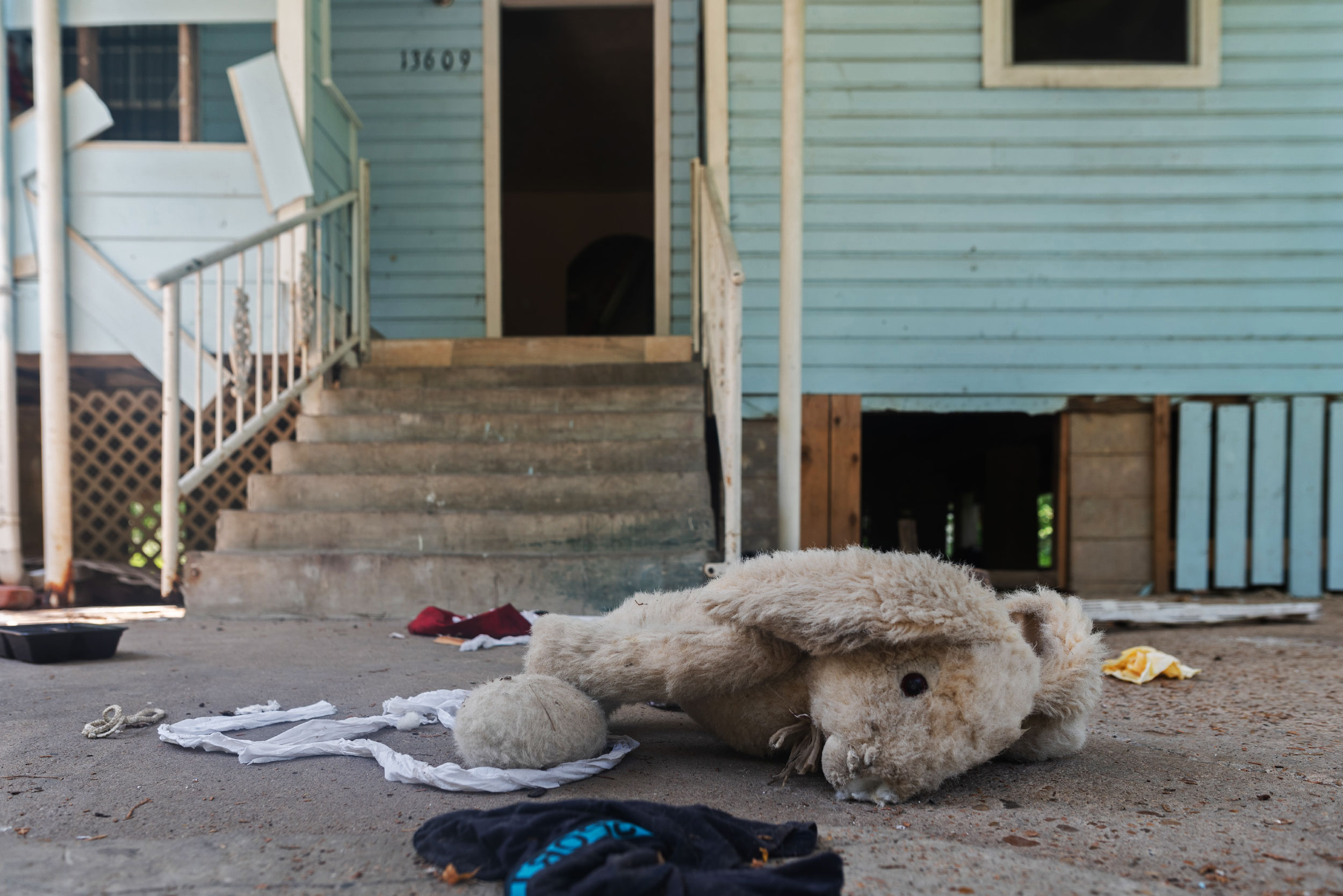 Clothes, food containers, and a tattered stuffed rabbit lie on the ground in front of an empty house in Allen Field.