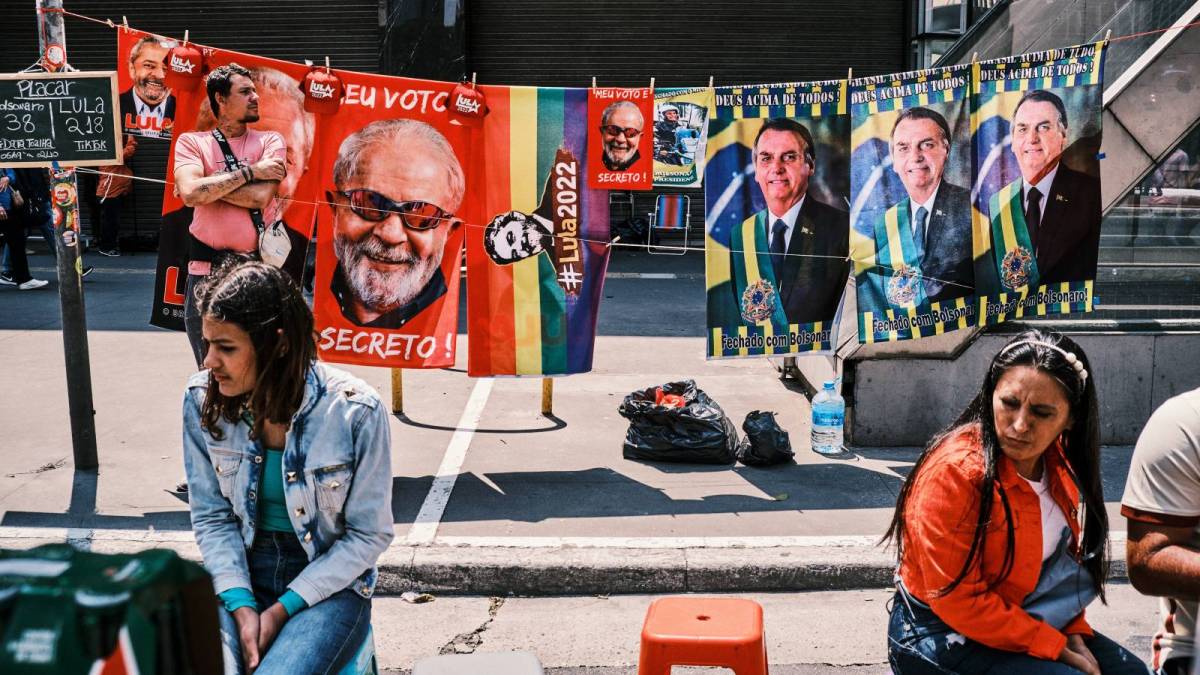 women sit on a bench in front of flags depicting support for Lula and Bolsonaro