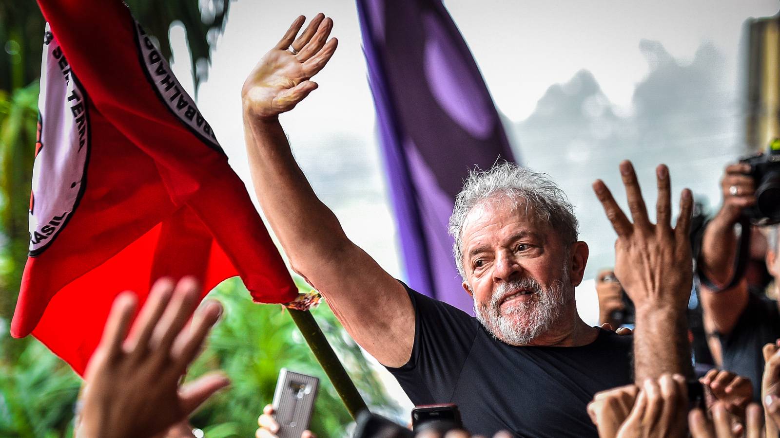 lula waves in front of flags with hands raising waving back at him