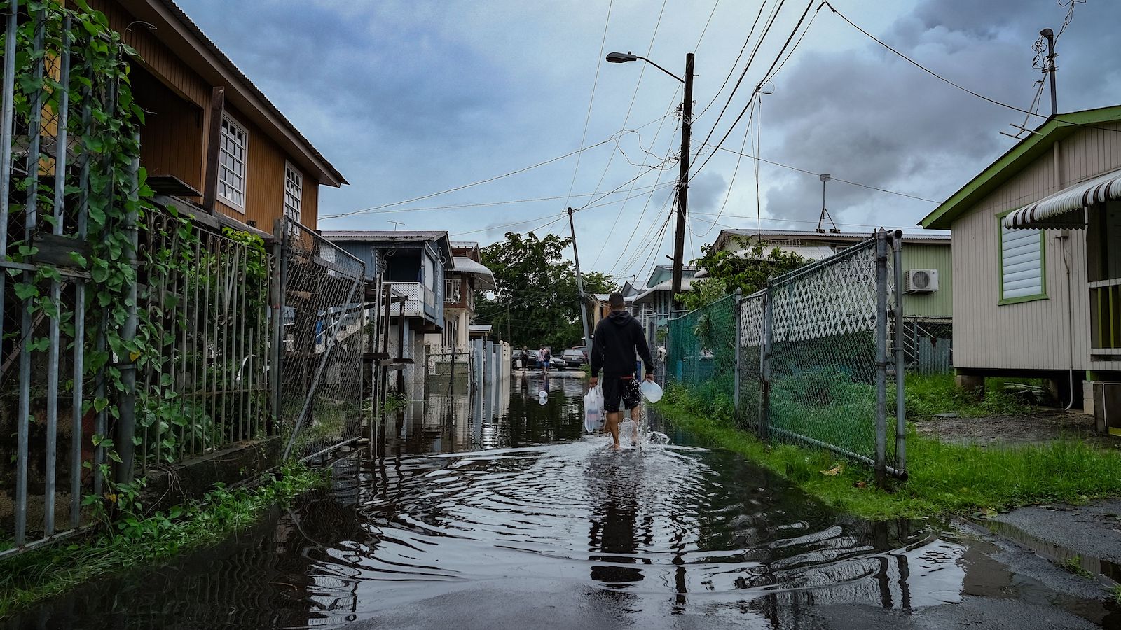 a man walks through a flooded street in between two houses