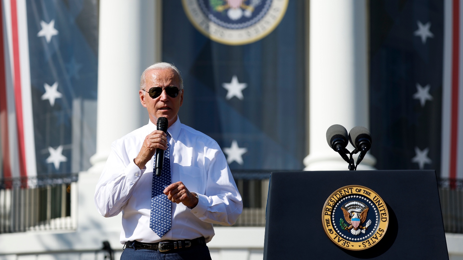 Biden speaks into a microphone against a stars-and-stripes themed backdrop