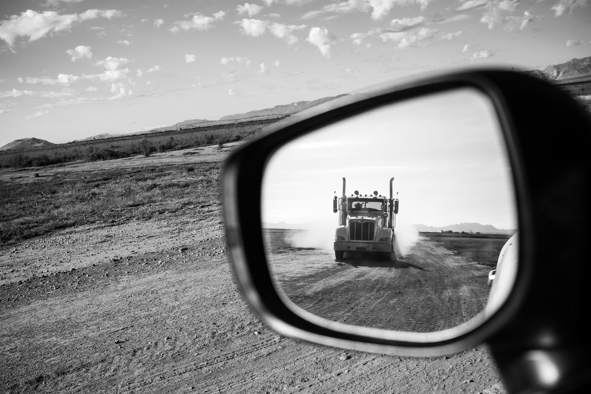 a rear view mirror shows a truck driving down a dusty road