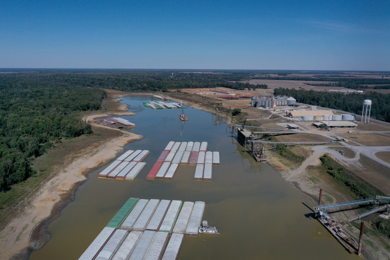 An aerial image shows various container ships sit in the Mississippi River, to the left is green vegetation and to the right is farm equipment
