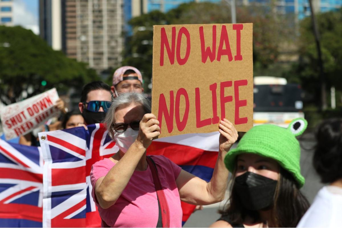 A woman wearing a face mask holds up a sign saying "no wai no life"