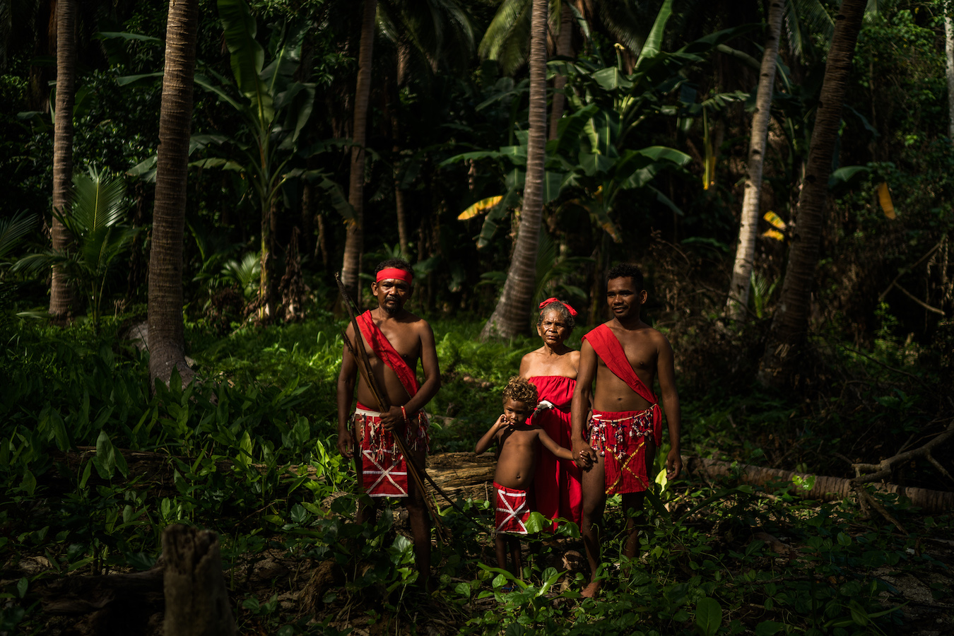 Four Indigenous people wearing red clothes stand in a forest