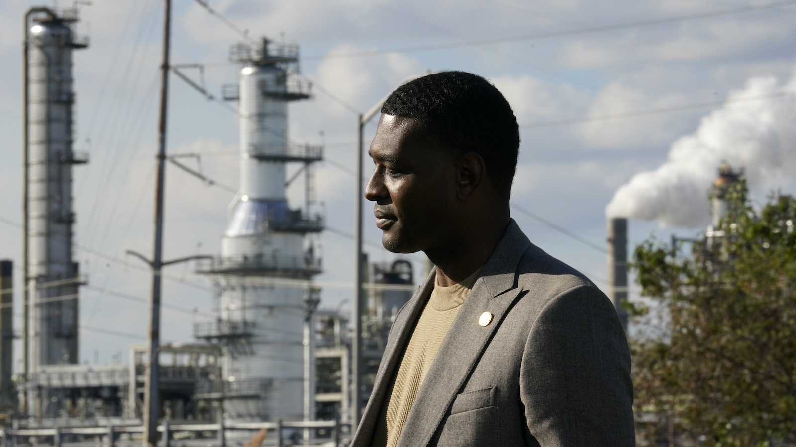 A man in a suit stands in front of industrial plant