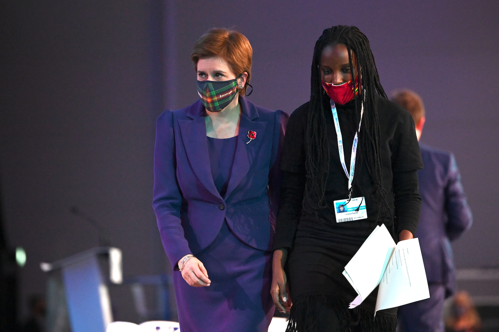 two women, one in a purple suit, the other in black, walk through a conference room