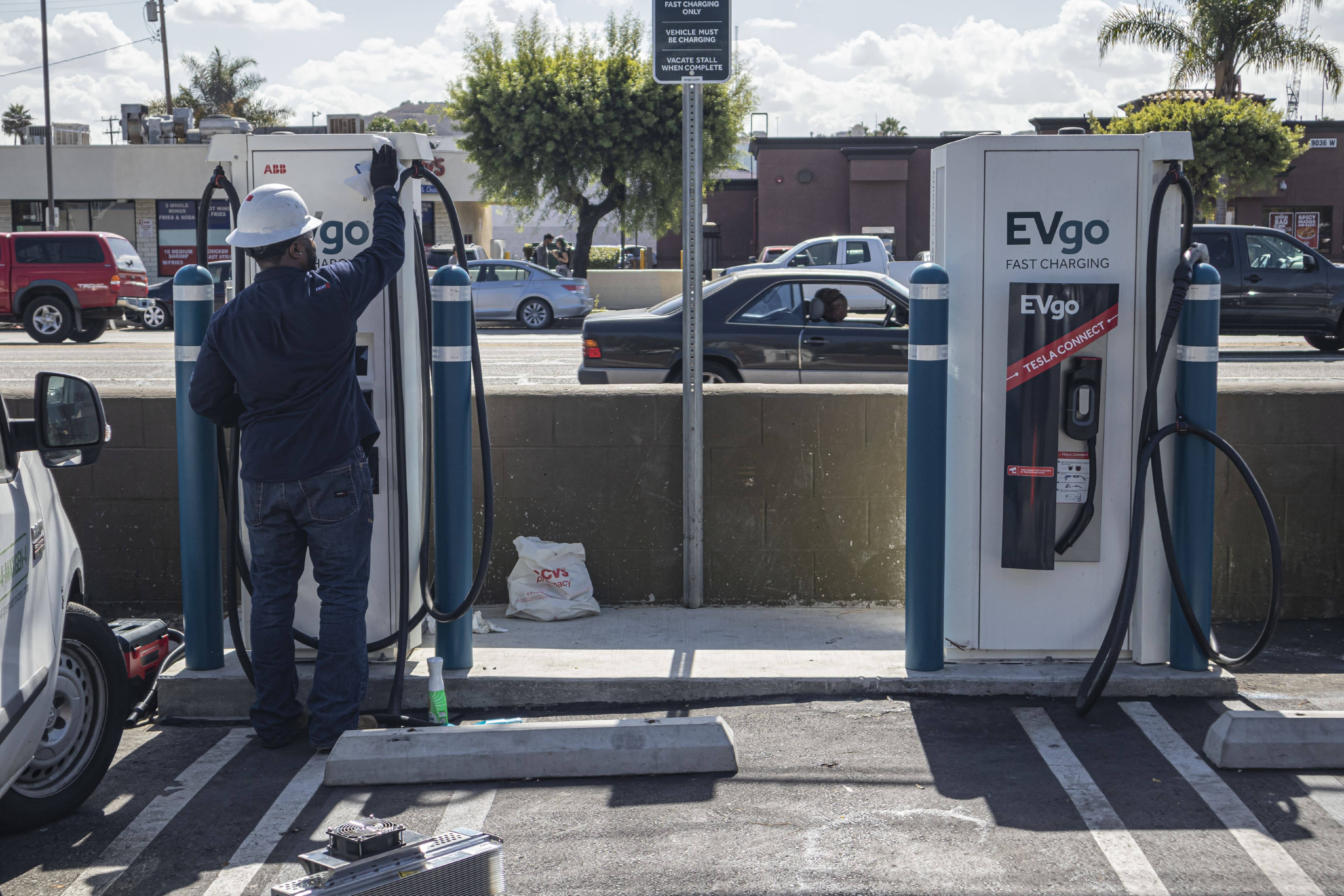 a person with a hardhat cleans an electric vehicle charing station