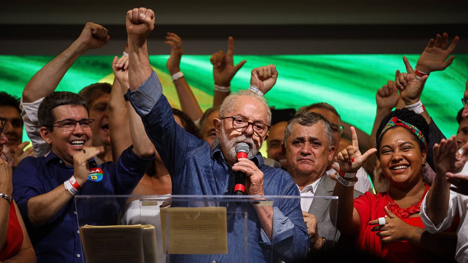Luiz Inacio Lula da Silva gives a press conference standing at a podium with his fish in the air and a crown behind him