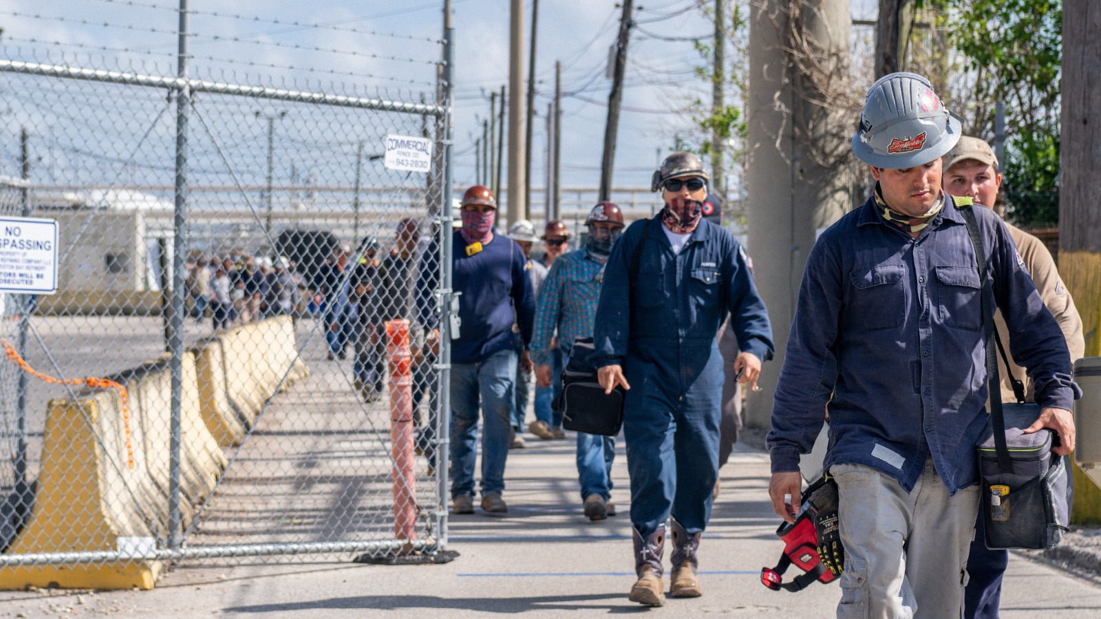 Men in hard hats and boots exit an industrial area in a line.
