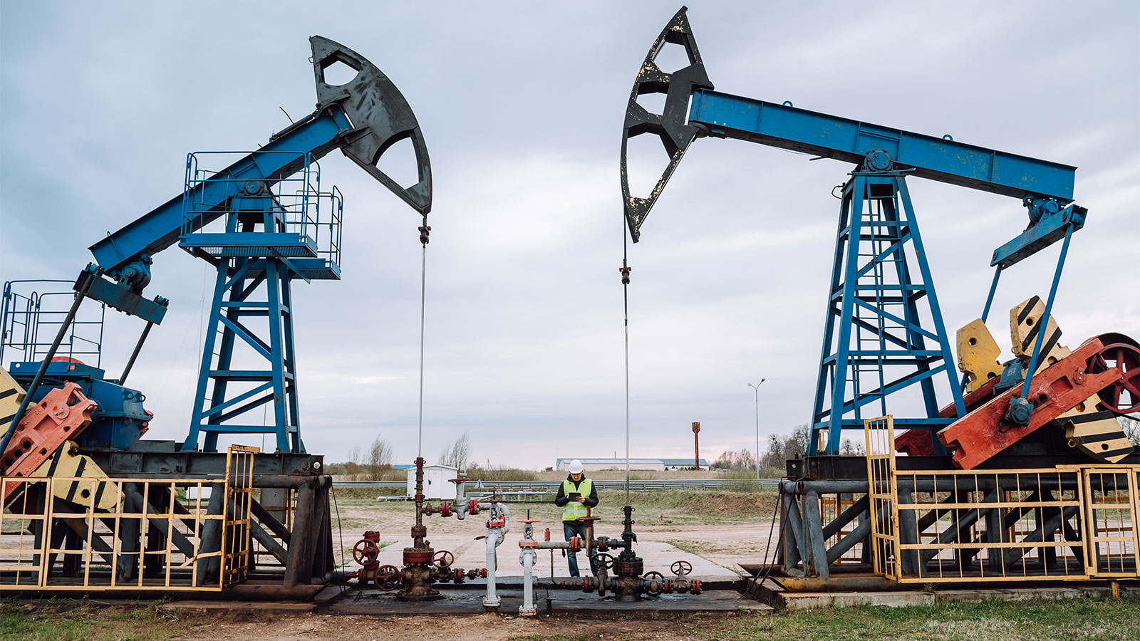 A worker standing between two giant blue oil pumpjacks