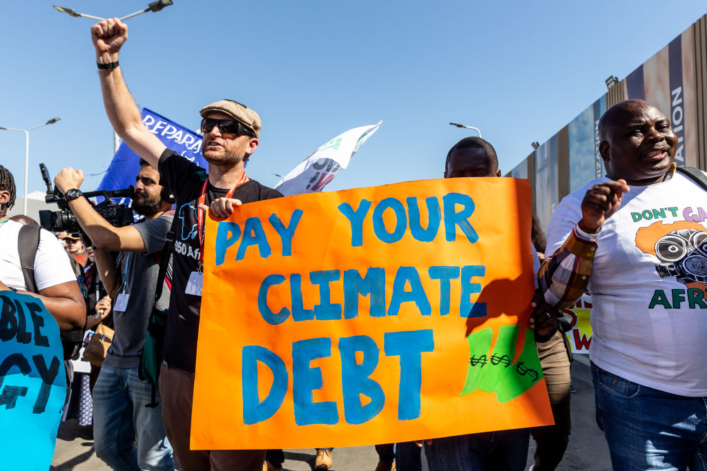 Activists hold sign stating "Pay your climate debt"