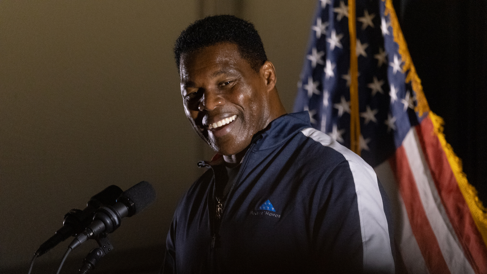 Herschel Walker smiles in front of a microphone