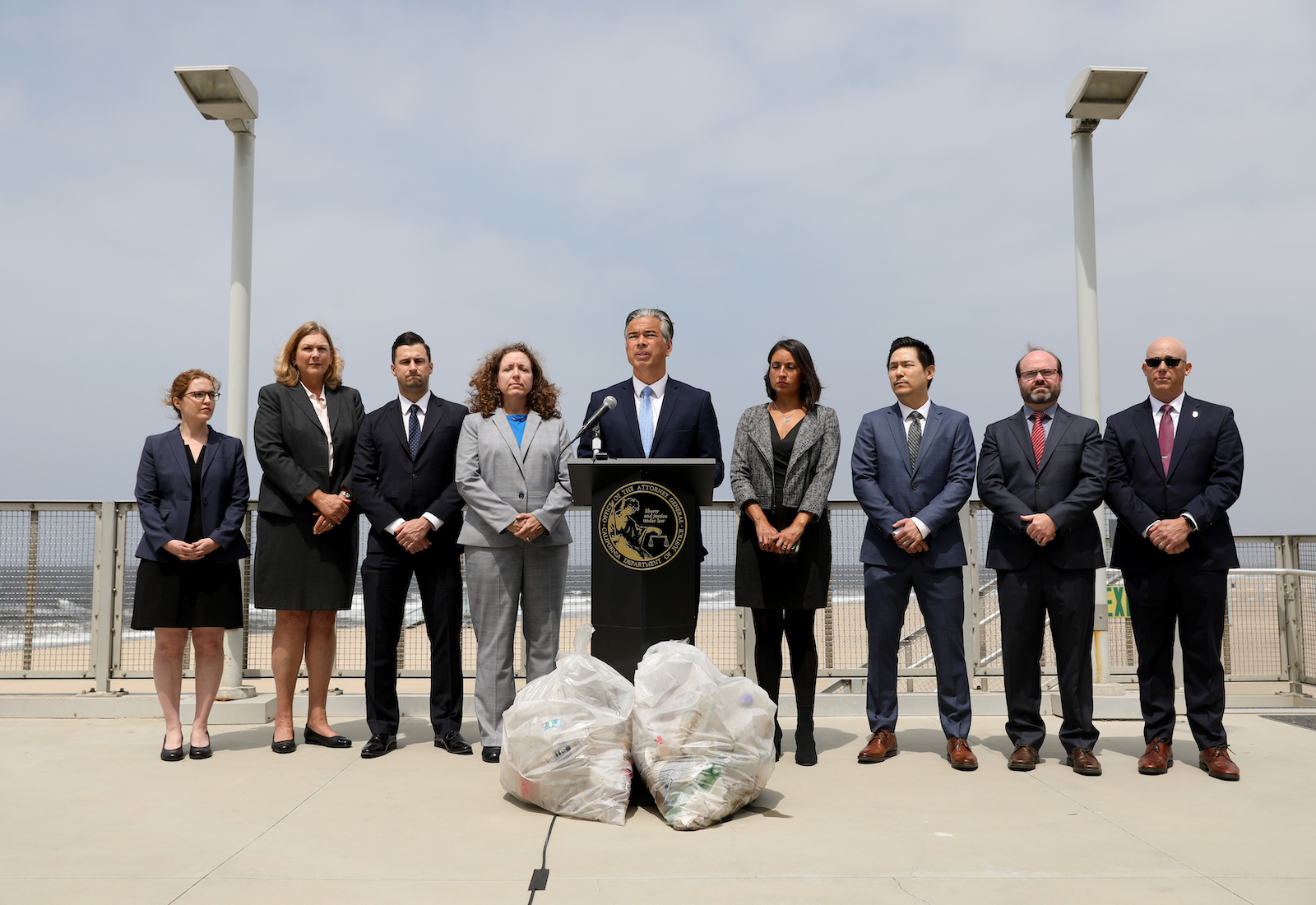 Attorney General Rob Bonta and his legal team stand on a beach with plastic bags in front of them