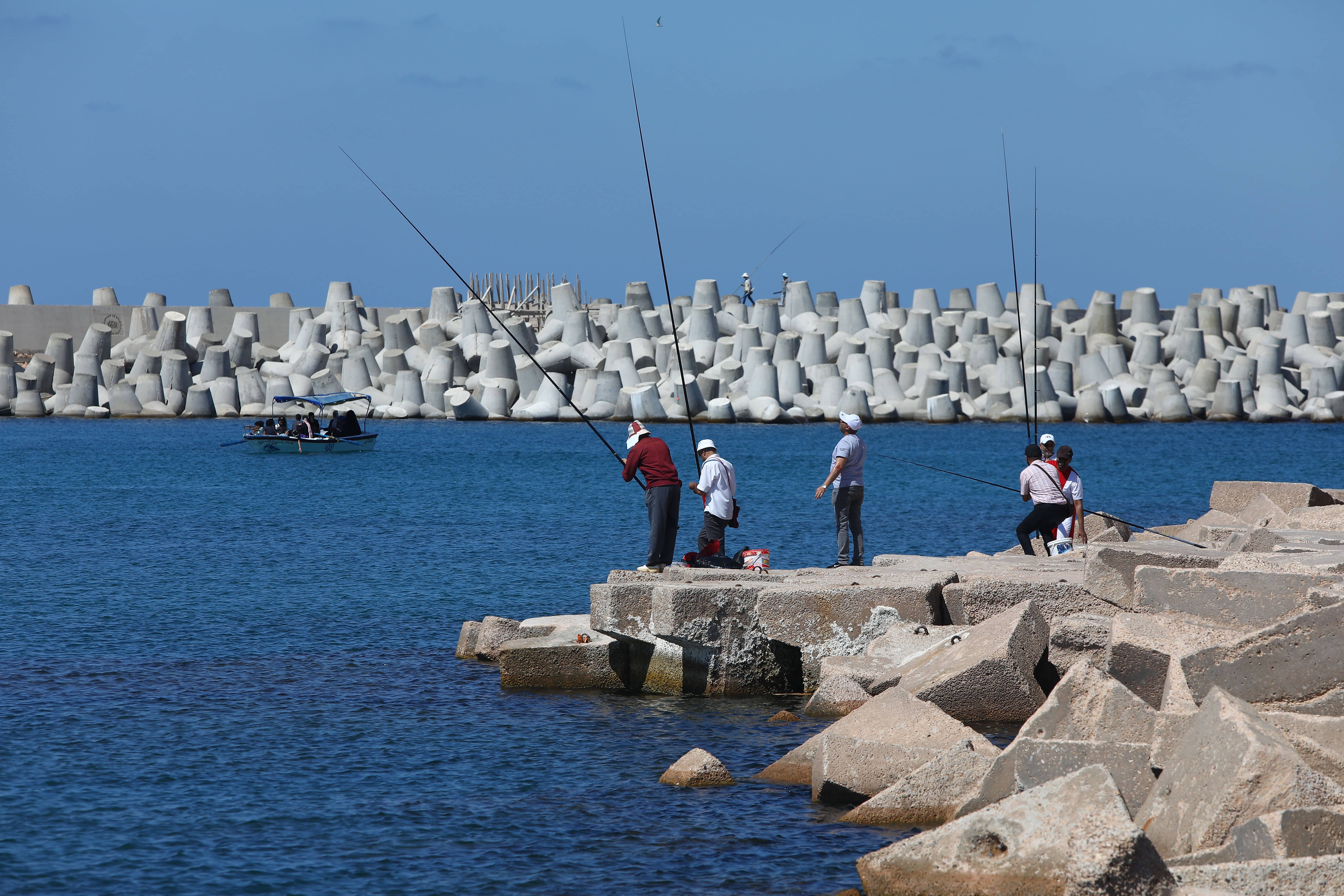 people fishing standing on a sea wall with another sea wall on the background