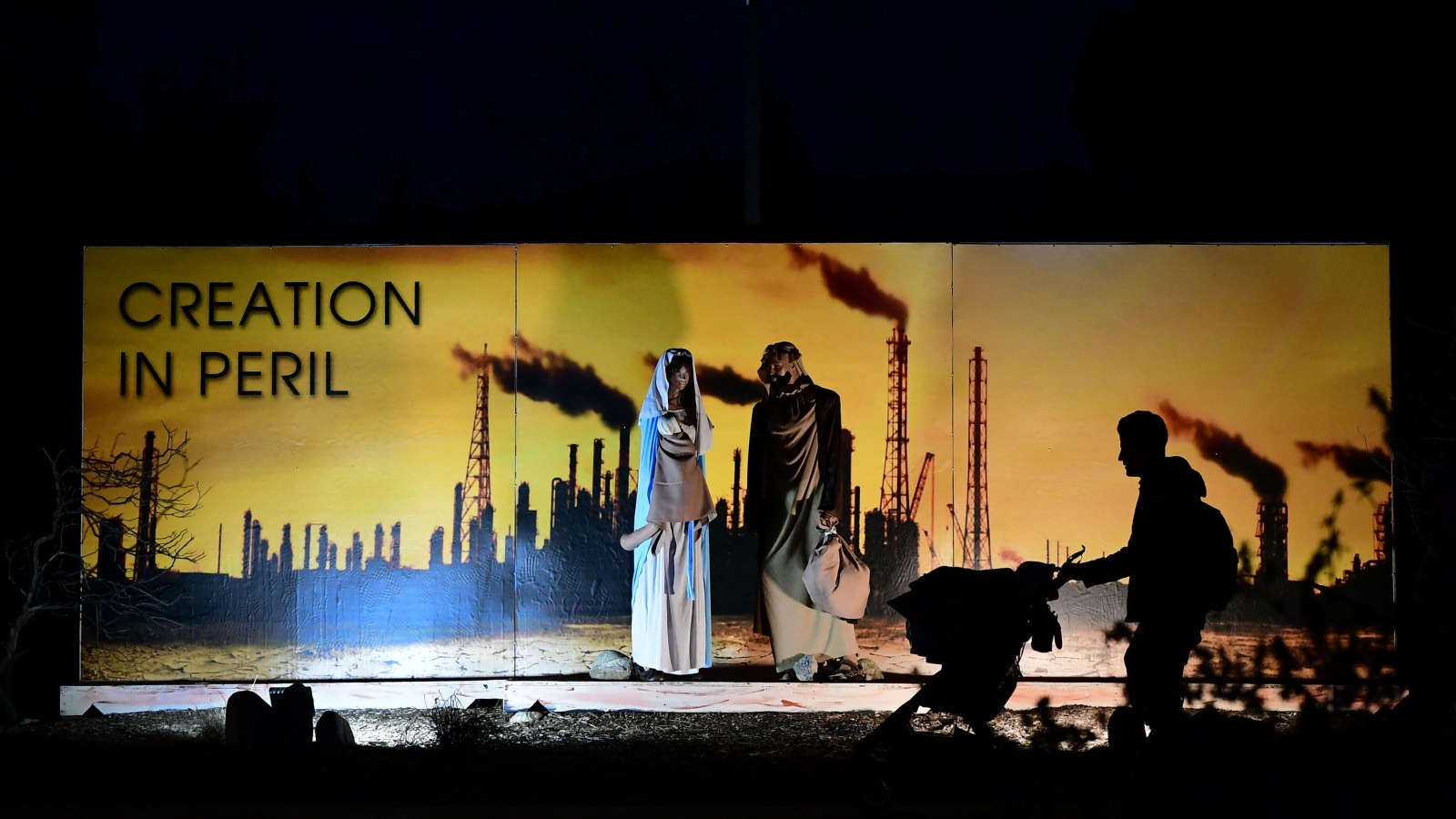 A nativity scene in front of a sign showing pollution and saying 