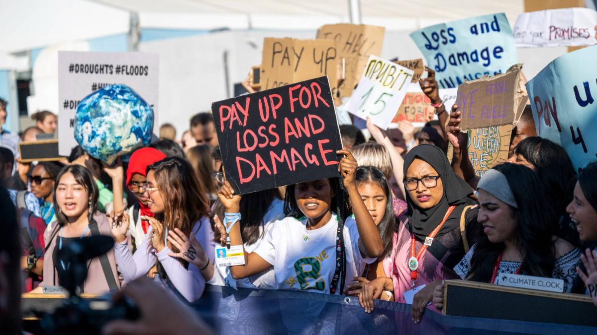 protestors hold up signs calling for wealthy countries to pay for loss and damage