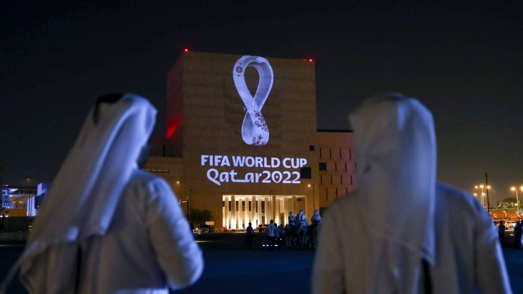 People gather to look at logo of 2022 FIFA World Cup projected onto building.