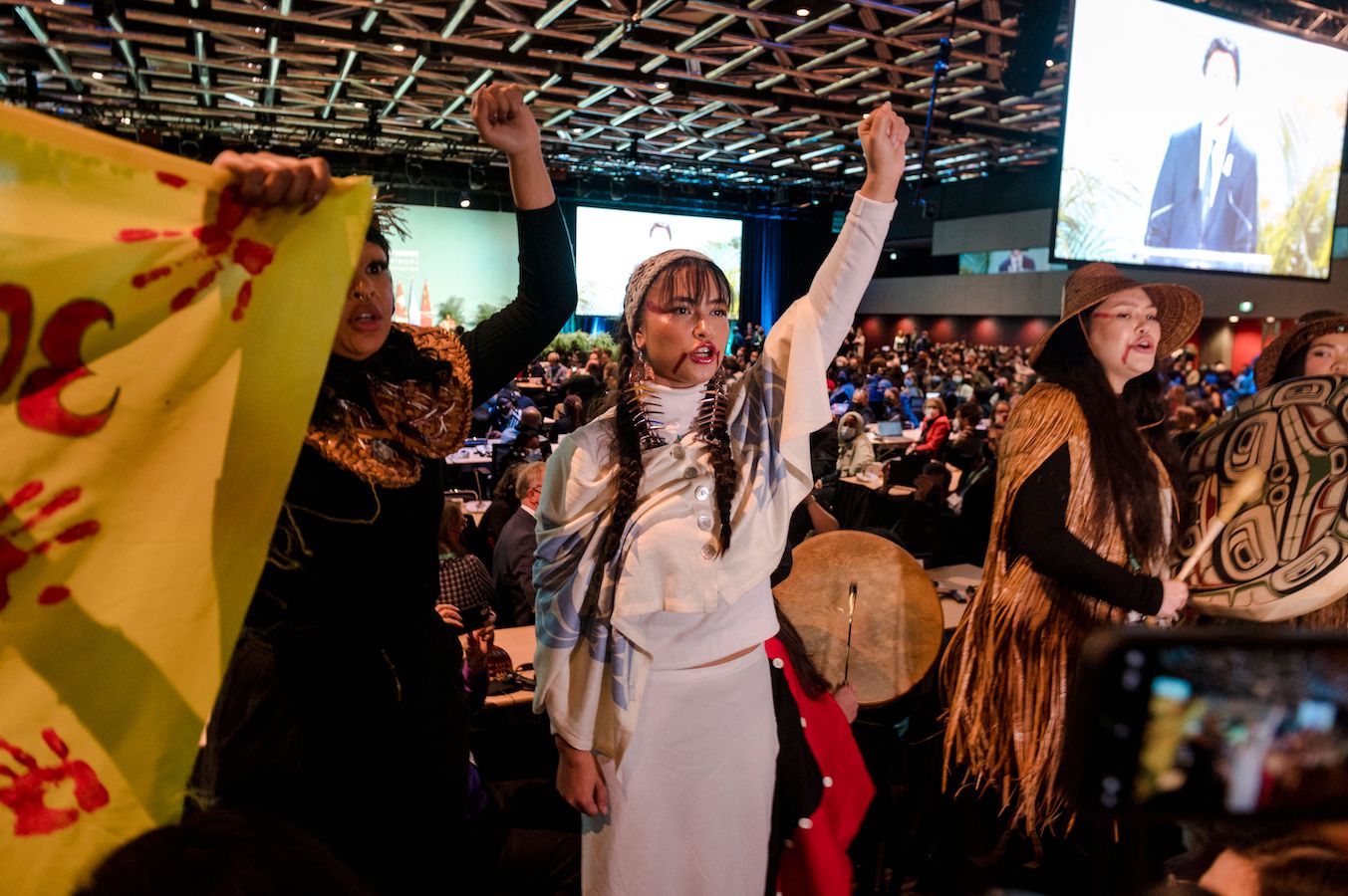 Indigenous protestors raise their fists in a large conference room