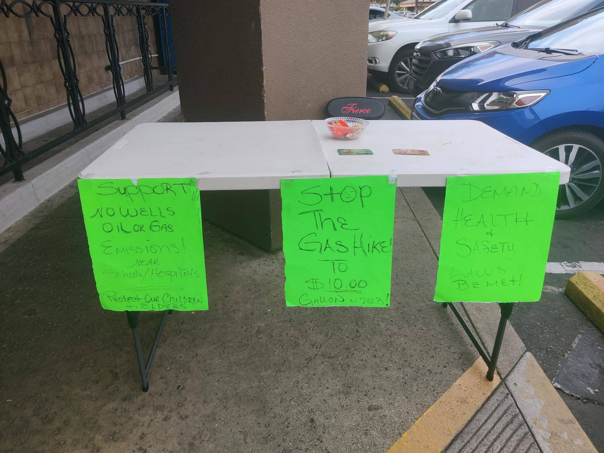 a table in a parking lot with signs attached reading "demand health and safety" and "stop the gas hike"