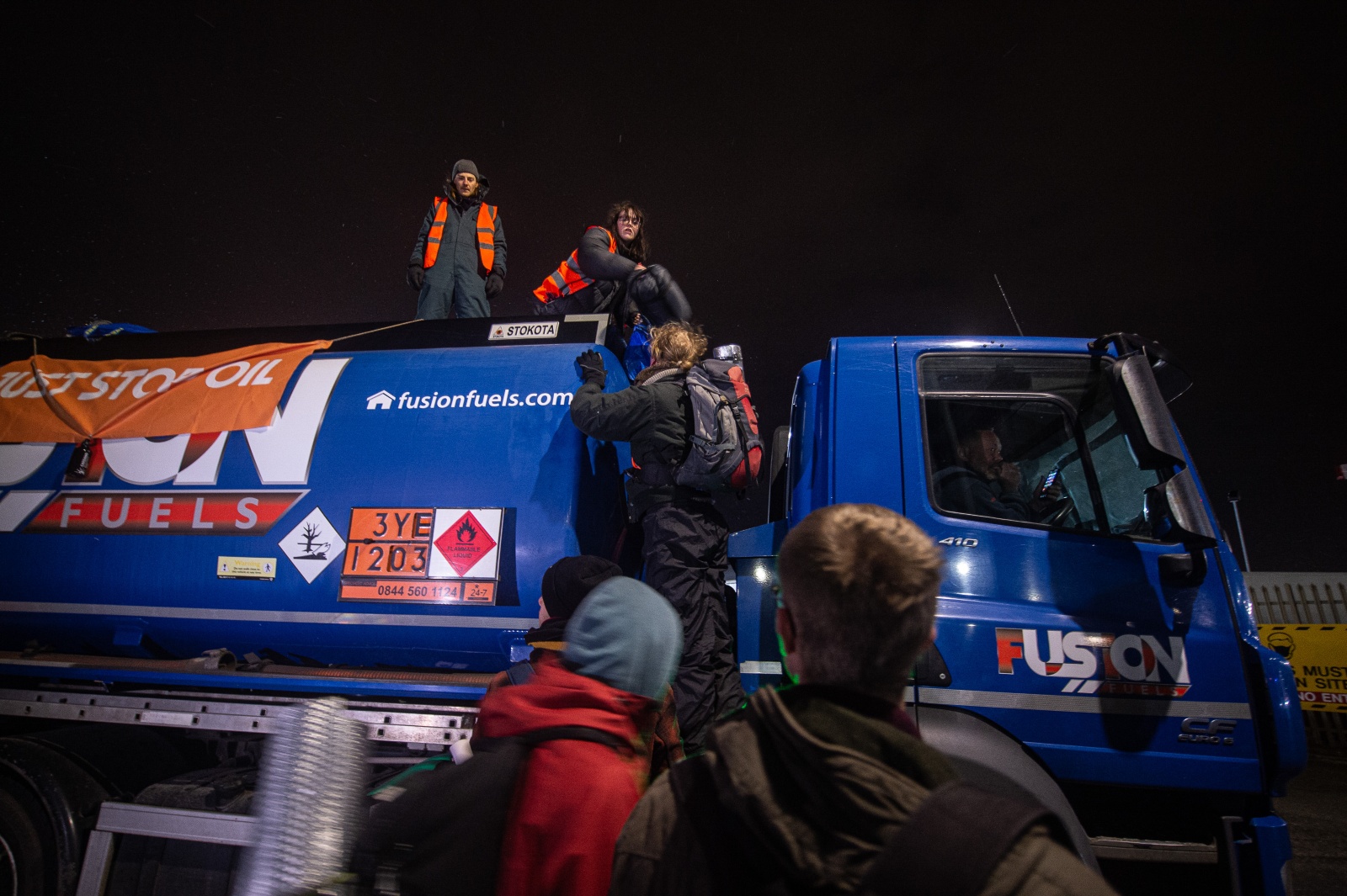 People climb on top of a fuel truck at night.
