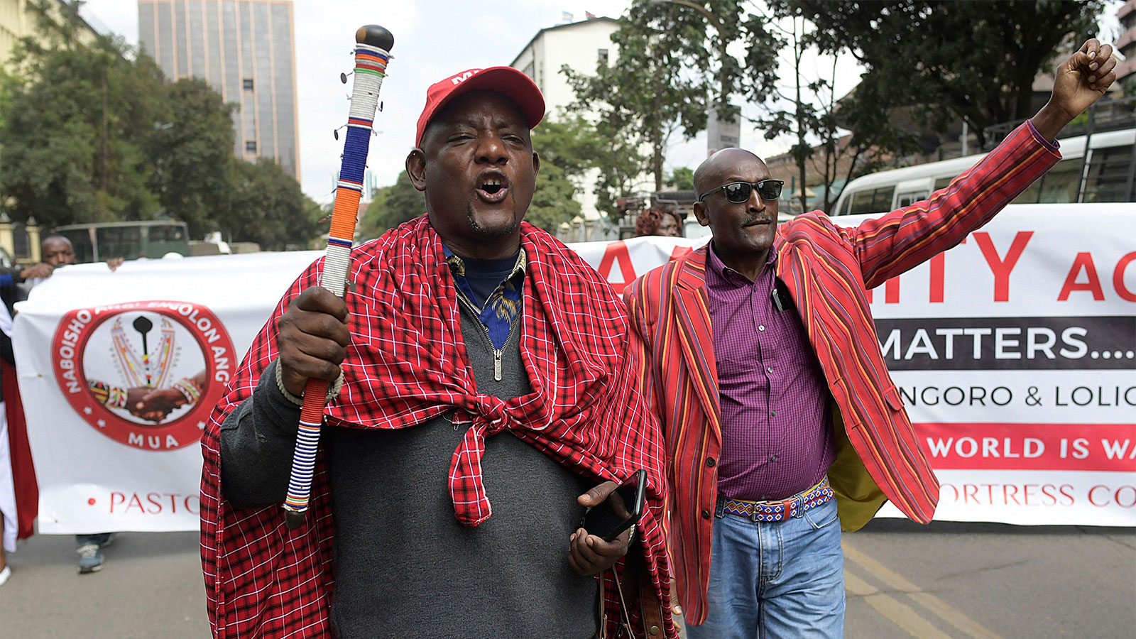Two people protesting the forceful eviction of the Loliondo Ngorongoro Maa community by the republic of Tanzania; a banner is held by others behind them