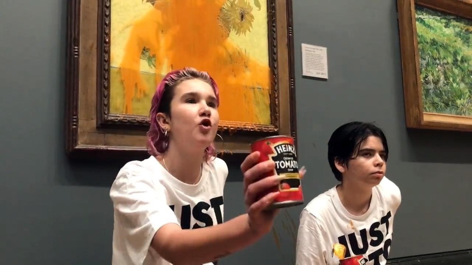 Two protesters in Just Stop Oil T-shirts are glued to a wall next to a painting covered with soup.