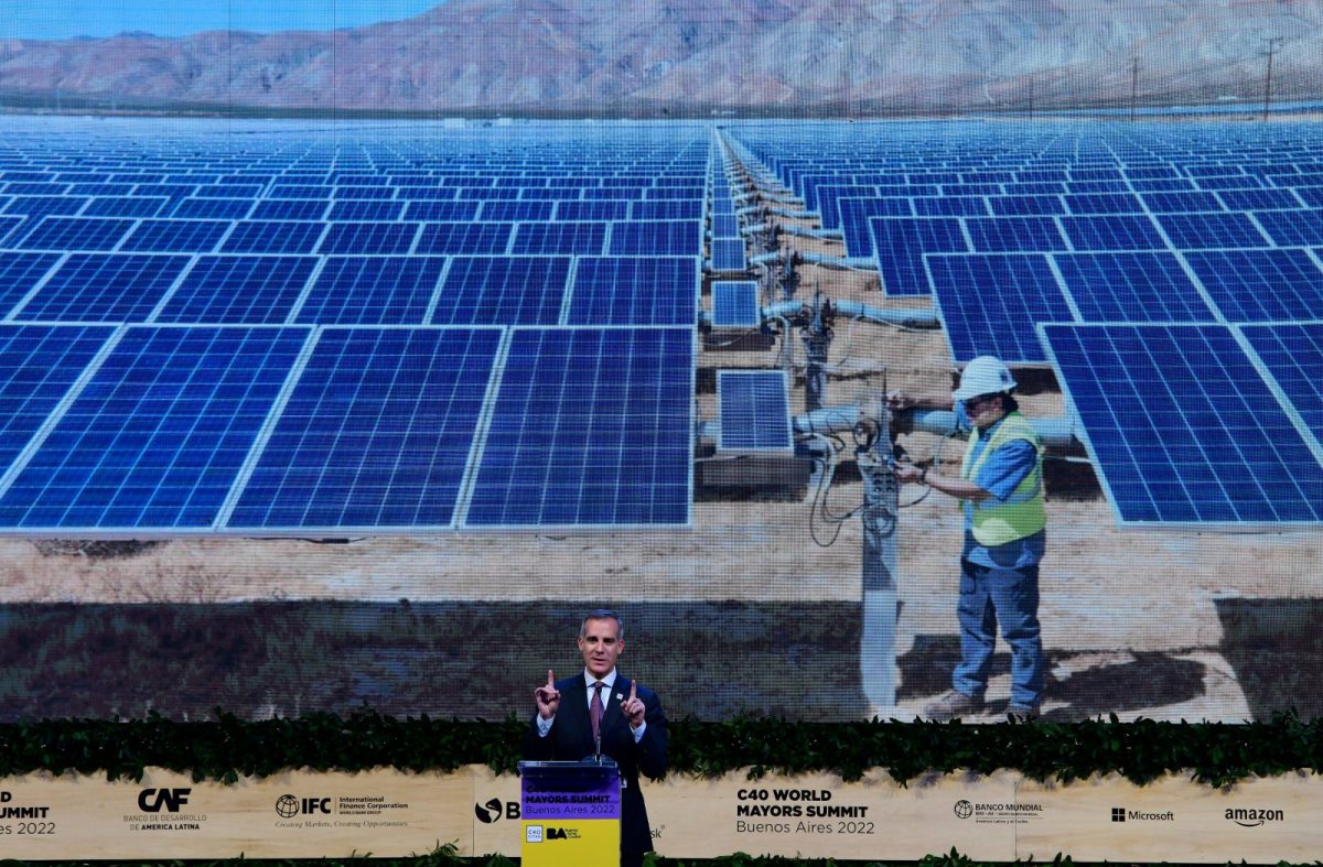 Former Los Angeles Mayer Eric Garcetti speaks in front of a large screen showing a field of solar panels, at the C40 summit in Buenos Aires.