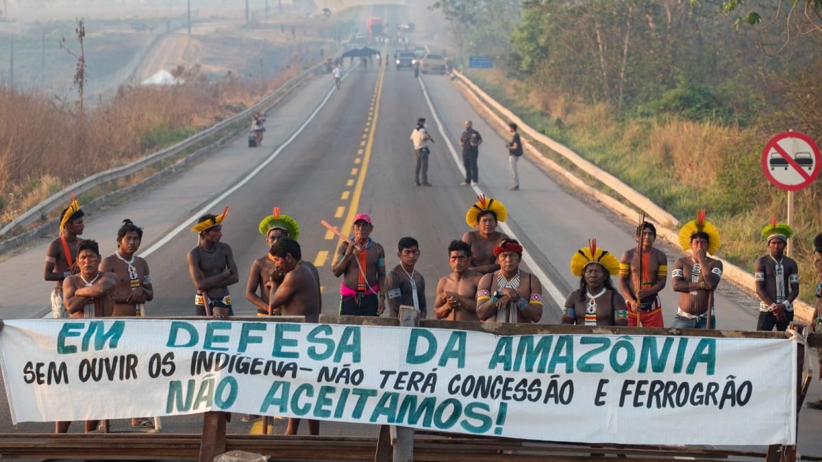 Kayapo Indigenous protesters block highway BR-163 in Brazil with a banner that reads in Portuguese: "Defending the Amazon. Without listening to Indigenous people, there will be no concession and no grain railway."