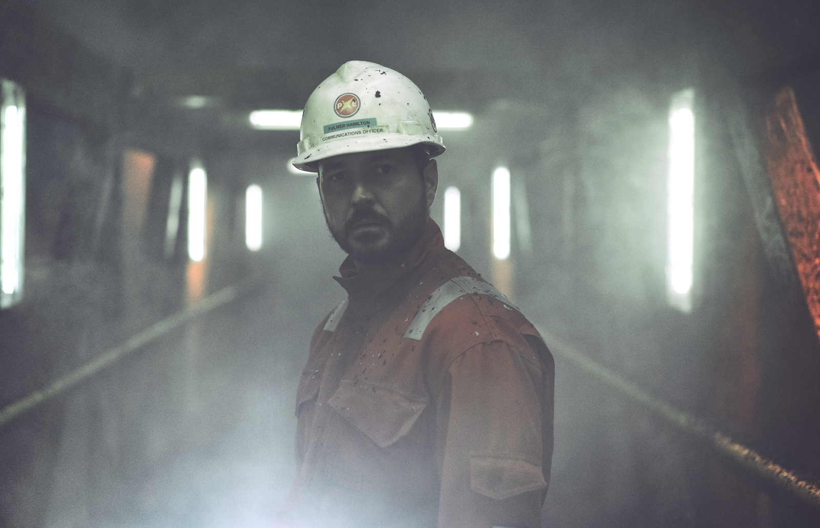 a man in a red-orange jumpsuit stands in a foggy hallway