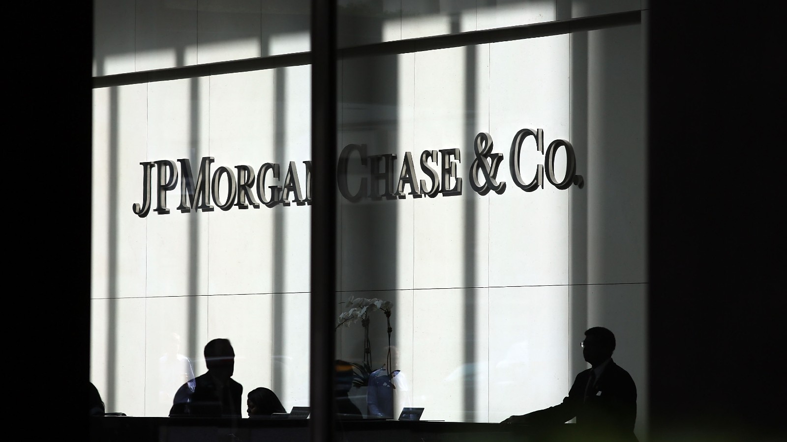 a photo of JPMorgan offices with people standing inside covered in shadow, company name is on the wall