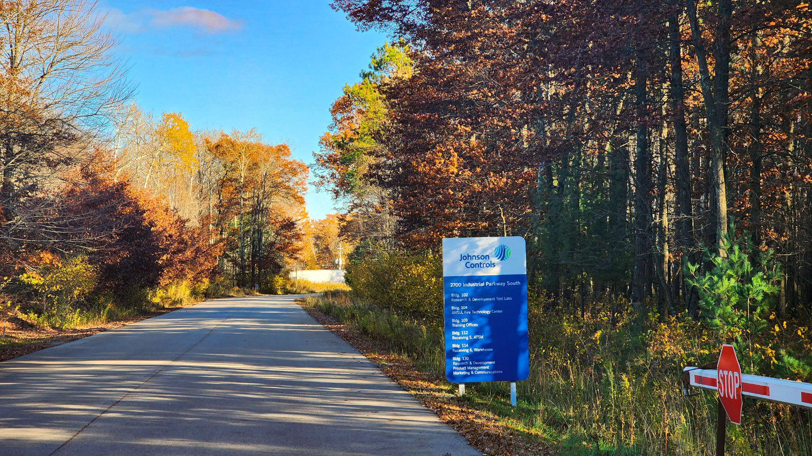 Road with autumnal trees on either side and a sign for Johnson Controls' facility
