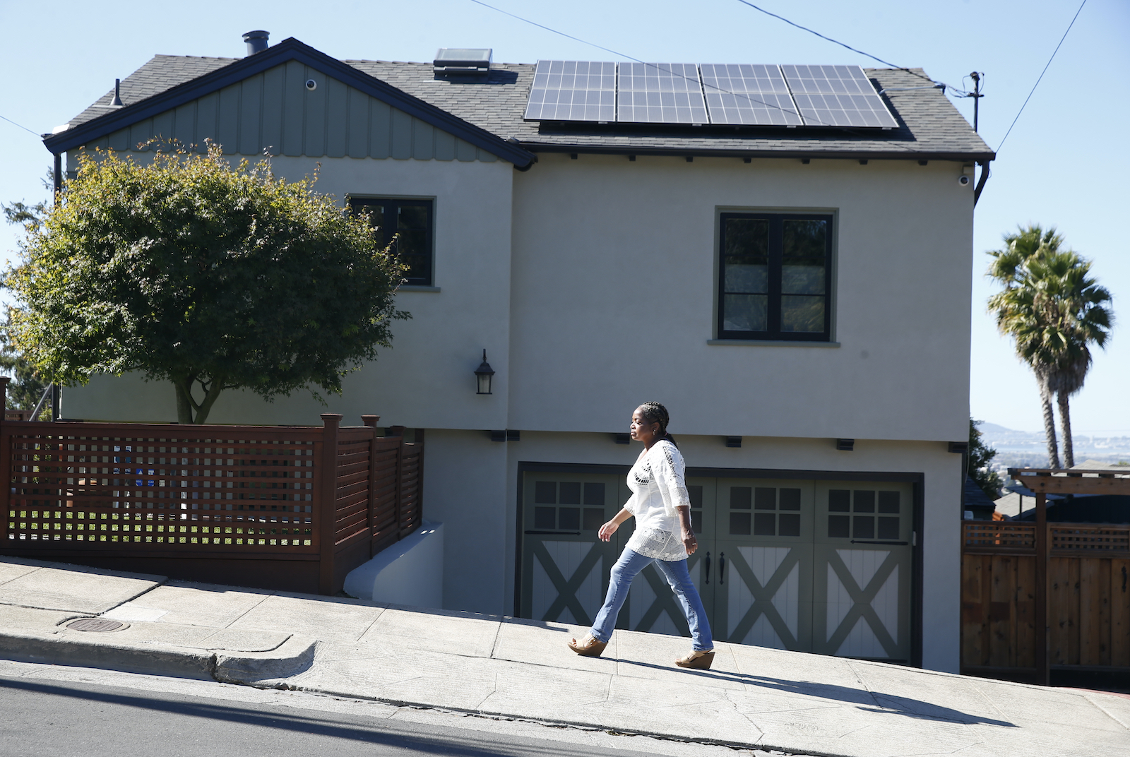 A woman walks past a home with solar panels installed on the roof in Oakland, California.